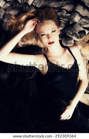 Stunning young woman with beautiful blonde hair lying on furs. Luxury, rich lifestyle. Jewellery. Fashion shot.