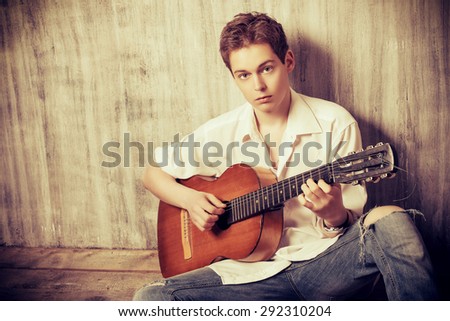 Romantic young man playing an acoustic guitar, sitting on the wooden floor