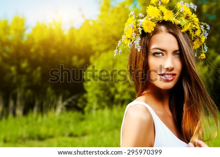 Romantic smiling girl in a wreath of wild flowers sitting on the lawn. Summer life. Beauty.