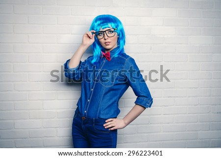 Modern girl wearing bright blue wig and jeans clothes posing by the urban white brick wall. Beauty, fashion.