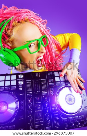Expressive modern DJ girl wearing bright clothes, headphones and bright dreadlocks mixing up some music. Disco, party. Modern generation.