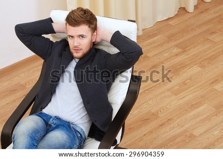 Dreamily thoughtful young man sitting relaxed on the armchair.