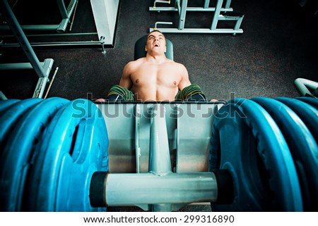 Muscular man weightlifter doing leg presses in gym. Sports.
