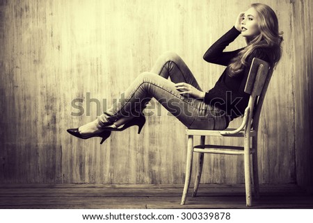 Black-and-white portrait of a beautiful blonde girl in jeans clothes posing by the grunge wall. Fashion.