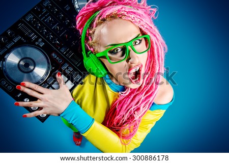 Expressive modern DJ girl wearing bright clothes, headphones and bright dreadlocks mixing up some music. Disco, party. Modern generation.