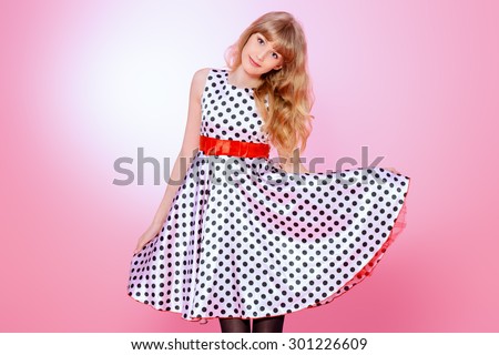Portrait of a pretty teenager girl posing in pin-up dress over pink background. Beauty, fashion.