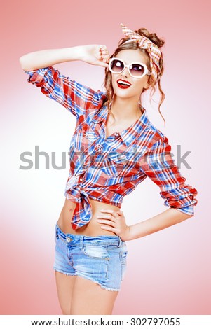 Pretty pin-up girl alluring in shorts and shirt over pink background. Beauty, fashion. Optics, eyewear.