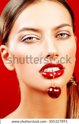Attractive young woman eating fresh cherry. Sexual lips, red lipstick. Healthy food concept. Cosmetics. Red background.