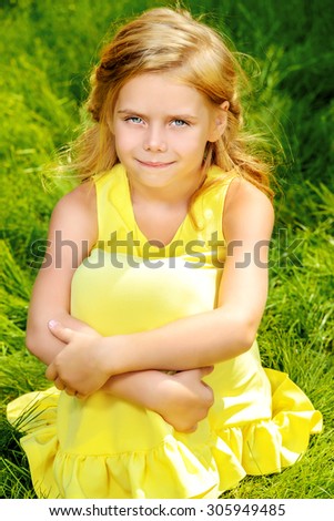 Pretty little girl sitting on a green lawn in summer day and smiling.