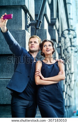Beautiful man and woman walking on the street and making selfie by smart phone. Fashion.