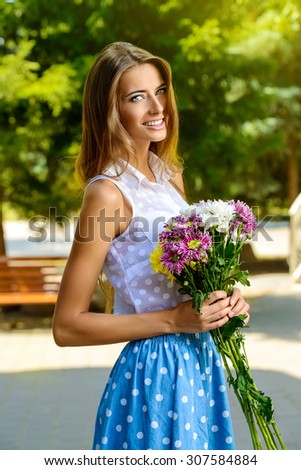 Happy smiling girl with bouquet of flowers standing outdoor. Summer day.