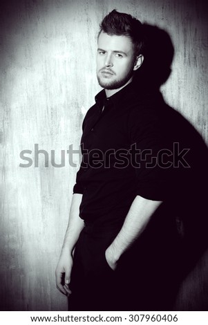 Black-and-white portrait of a fashionable man in black shirt posing at studio. Men\'s beauty, fashion.