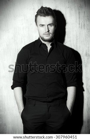 Black-and-white portrait of a fashionable man in black shirt posing at studio. Men\'s beauty, fashion.