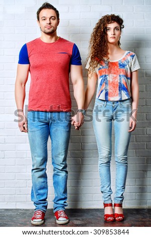Full length portrait of a casual young people standing by the brick wall. Jeans style. Relations. Love concept.