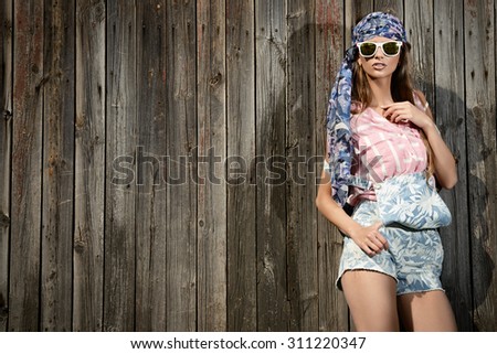 Beautiful romantic young woman in casual summer clothes stands by the old wooden fence. Outdoor fashion. Jeans style.