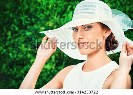 Portrait of a beautiful elegant woman in light white dress and hat standing in the summer park. Beauty, fashion.