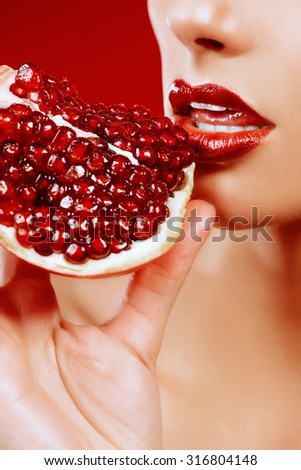 Attractive young woman eating fresh pomegranate. Sexual lips, red lipstick. Healthy food concept. Red background.