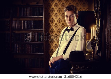 Elegant young man stands by the fireplace in a room with classic interior. Fashion shot.