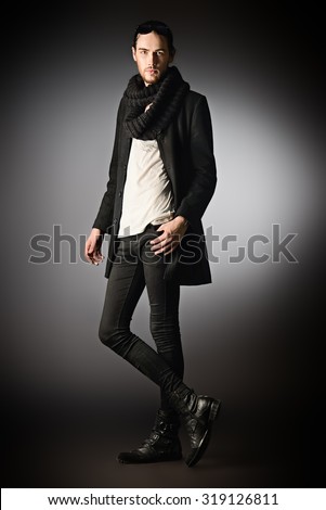 Fashion shot of a handsome male model in black suit posing in motion over gray background. Men\'s beauty.