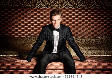 Handsome man in elegant suit sitting on a bed. Luxury. Vintage interior.