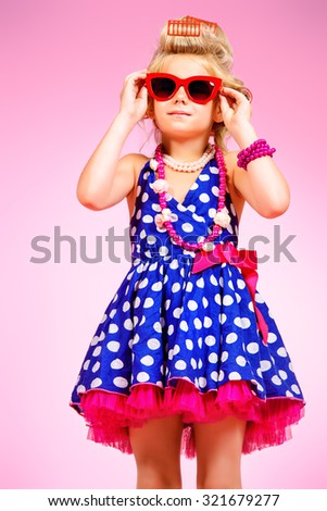 Fashionable little girl in her mother\'s hair curlers and pin-up sunglasses. Kid\'s fashion, cosmetics. Pin-up style.