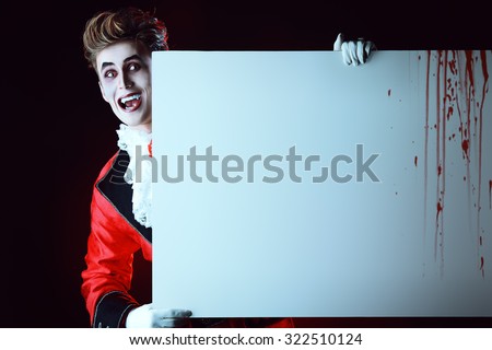Bewitching handsome male vampire holding a billboard with copy space. Halloween. Dracula costume.