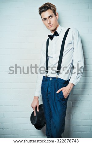 Portrait of a handsome young man in elegant suit posing by a white brick wall. Business.