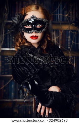 Charming mysterious girl in black mask and black medieval dress stands in a castle living room. Vampire. Halloween concept. Vintage style.
