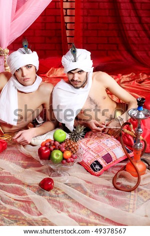Shot of two men in oriental costumes having a rest and smoking hookah.