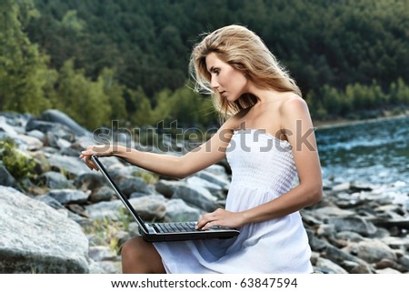 Happy young woman sitting  near the sea with a laptop.