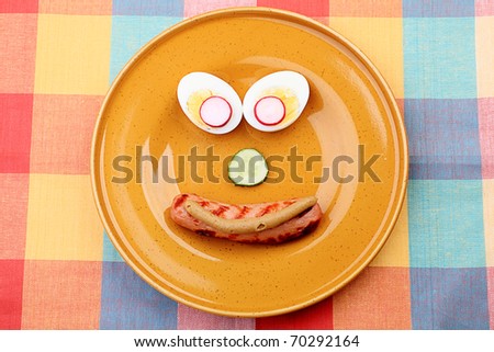 Shot of a dish with funny face made of fried sausage, egg and greens.