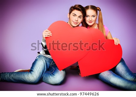 Happy young love couple posing together with red hearts.