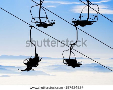 Ski lift chairs on bright winter day over the clouds
