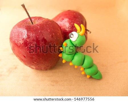 apple with a bite out of it showing a plasticine worm on brown paper background
