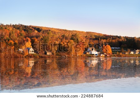 Rural scene during Fall or Autumn along the Saint John River in New Brunswick, with reflection of colorful trees along the water
