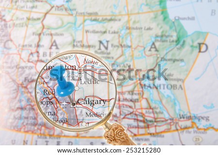 Blue tack on map of central Canada with magnifying glass looking in on Calgary, Alberta