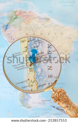 Blue tack on map of South America with magnifying glass looking in on Santiago, the capitol of Chile