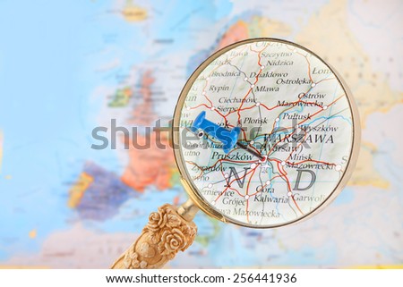Blue tack on map of Europe with magnifying glass looking in on Warsaw, Poland