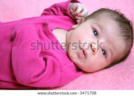 close up of a small one week old newborn baby expression on a pink background