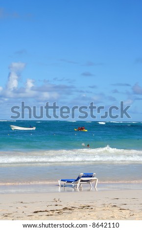 empty beach chair overlooking the ocean with boat on the Caribbean shore of Bavaro beach, Punta Cana in the Dominican Republic