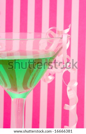 green martini with festive decorations like curled ribbons  with pink striped background