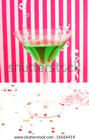 green martini with festive decorations like curled ribbons and confetti with pink striped background