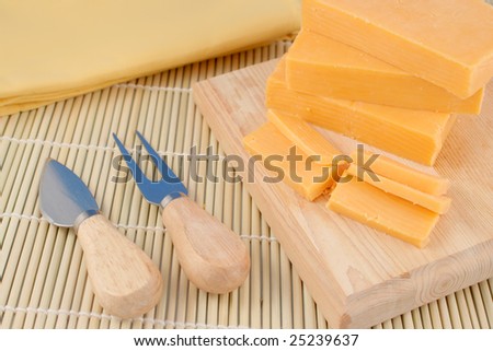 blocks of cheddar cheese on a wooden block with cheese cutting knife and accessories