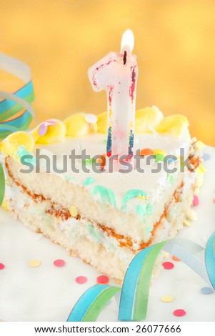 slice of first birthday cake with lit candle, confetti, and ribbon