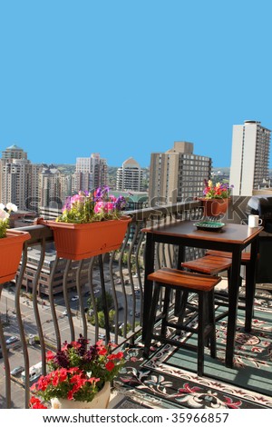 Rooftop patio with table and stool chairs, colorful flower baskets along a balcony railing with Calgary building skyline in the background