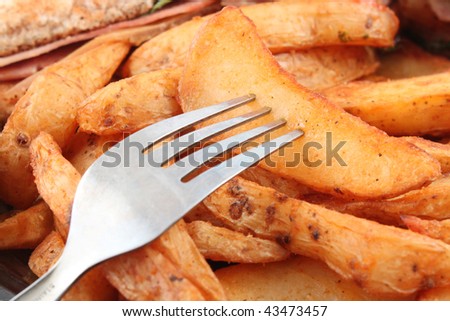 Closeup of fork and  golden fried spicy potato wedges (shallow depth of field)