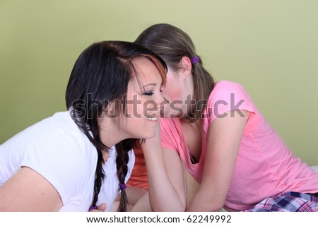 Two teenage girls have a slumber party or sleepover and one is whispering secrets in the other's ear
