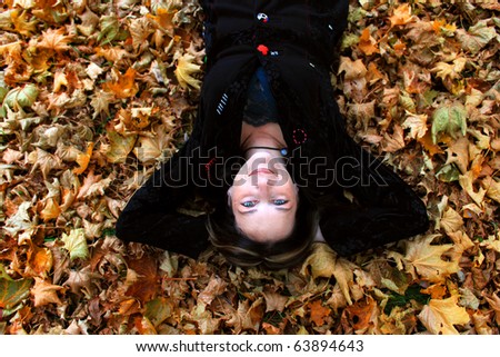 Beautiful woman in her forties is happily laying on the ground covered by a bed of autumn leaves