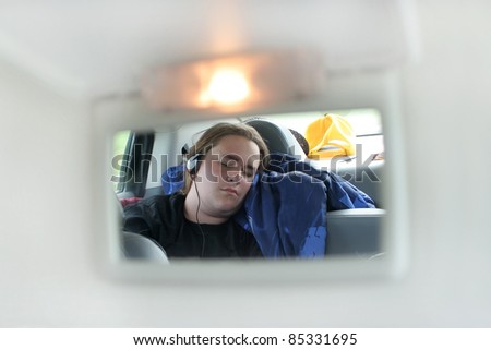 Teenage boy sleeps in the backseat of car on a roadtrip seen through the mirror or a sun visor