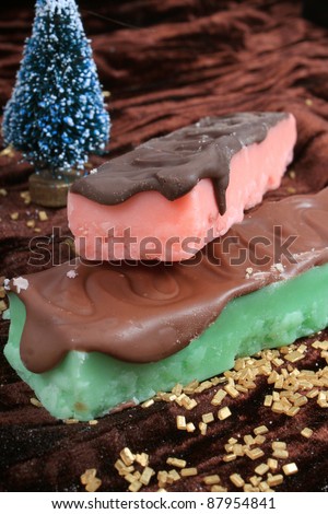 Strawberry pink, and mint green fudge bars covered in chocolate with gold flakes and christmas tree in the background